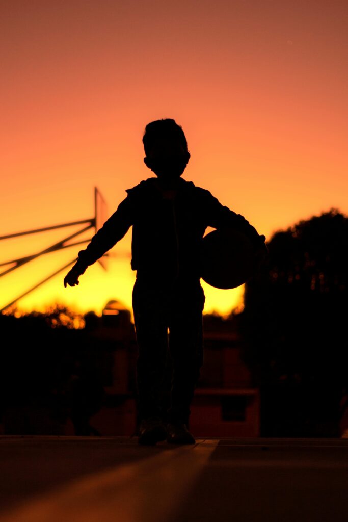 pexels-photo-12252288-12252288 A child with a basketball silhouetted against a vibrant sunset, capturing the beauty of San Andrés Cholula, Mexico.