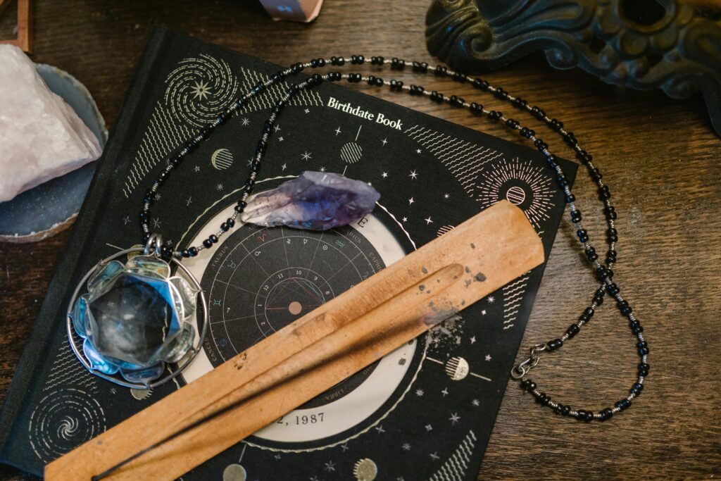 pexels-photo-6806400-6806400 Astrology-themed flat lay featuring a birthdate book, crystals, and necklace on a wooden surface.
